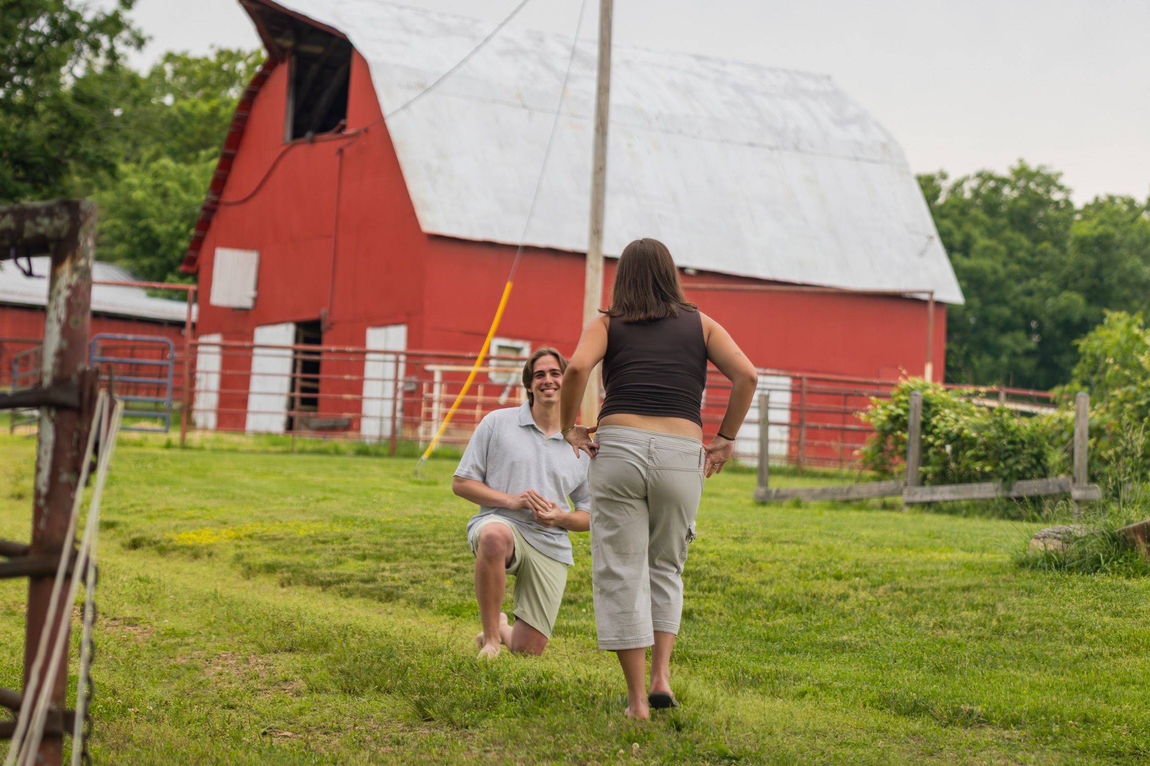 Andrew kneeling in front of Grace in the grass by a red barn
