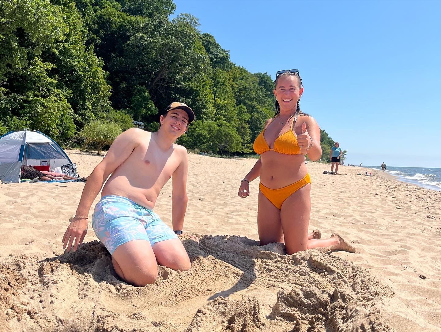 Andrew and Grace kneeling beside a sandcastle on a beach