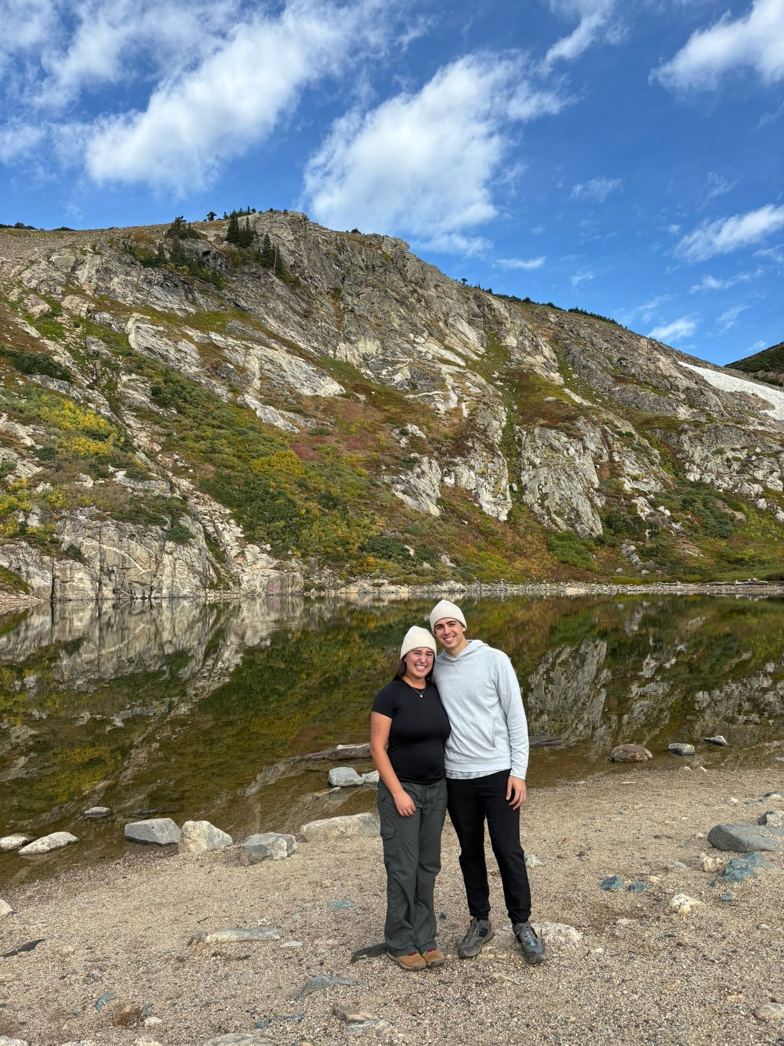 Andrew and Grace on a rocky shore below a mountain and a blue sky