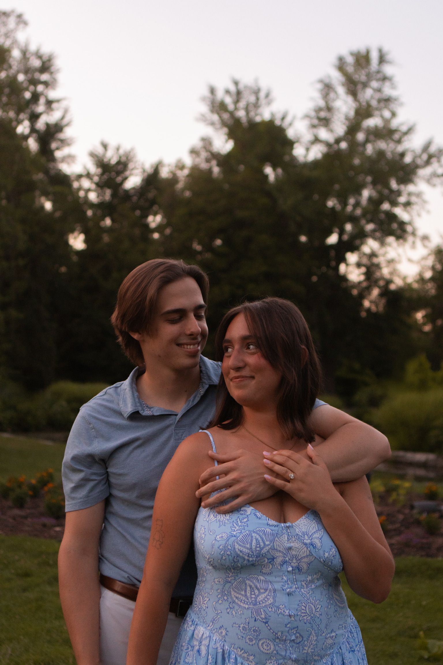 Andrew and Grace embracing in front of a line of trees at sunset